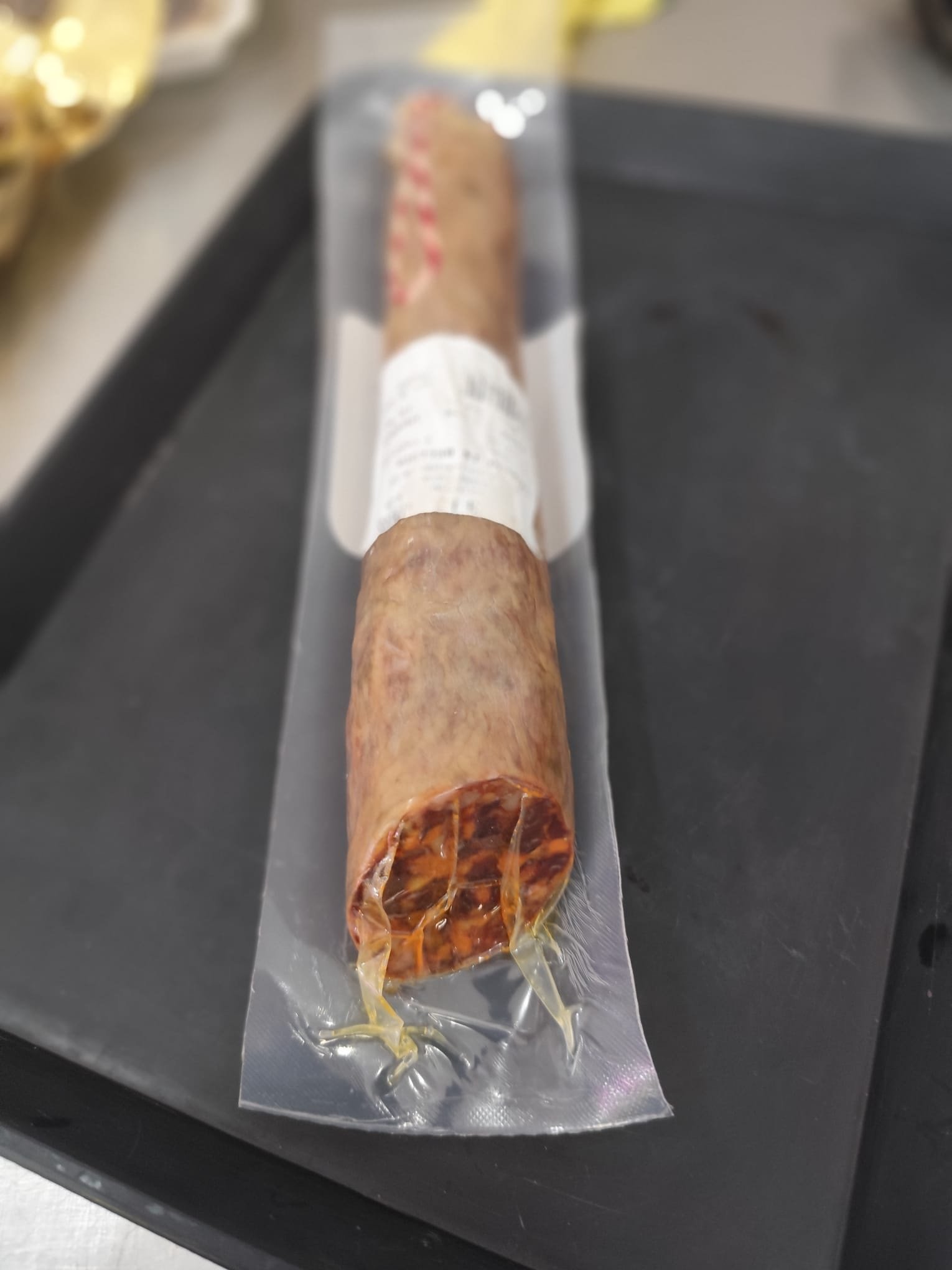 Medio chorizo cular extremeño curado, envasado al vacío, sobre bandeja negra